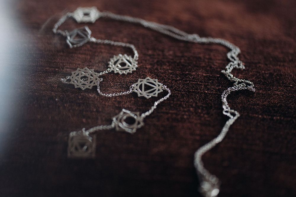 An elegant silver necklace with ornate details lying on a dark wooden surface.