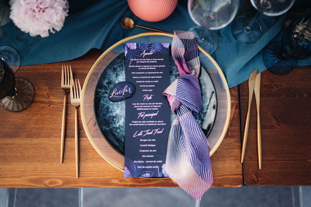 Wedding menu and place setting with navy and purple colors on wooden table with gold cutlery.