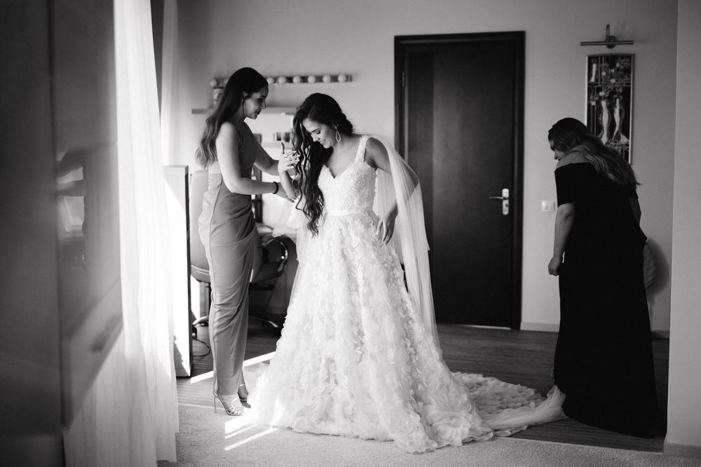 A black and white photo showing the final touches being made to an intricate lace wedding dress.