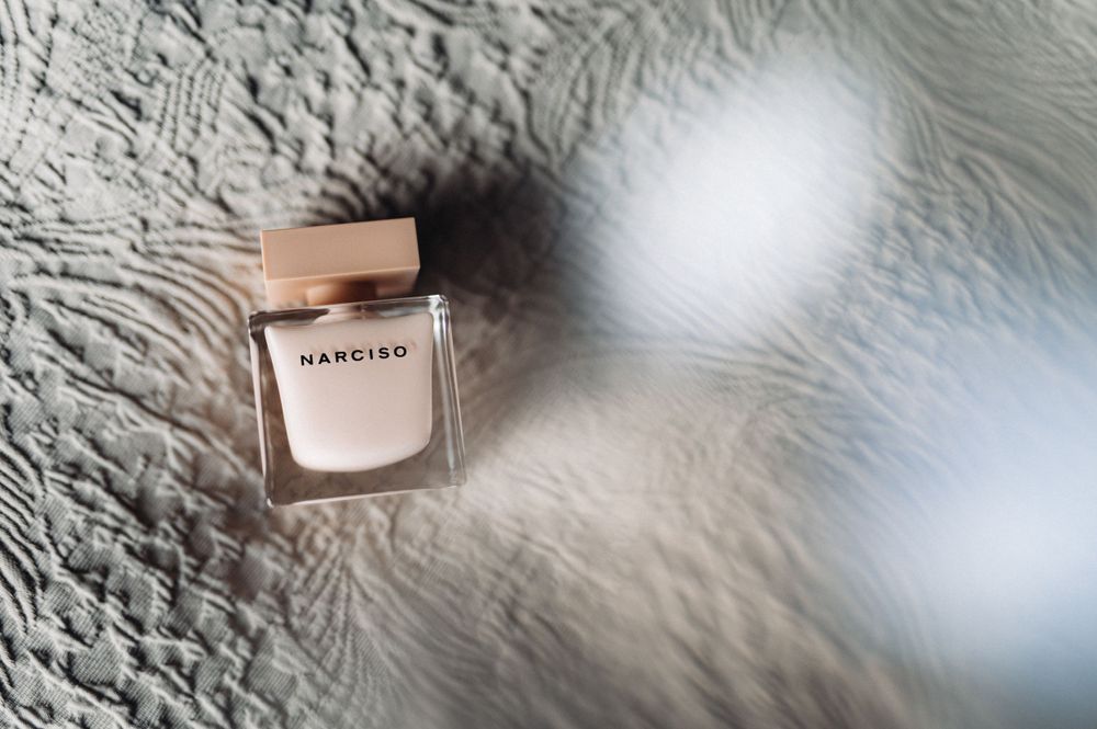 A delicate glass perfume bottle photographed on a textured white surface with soft lighting.