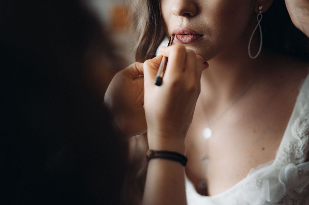 Wedding makeup artist applies lipstick to bride during final beauty preparations.