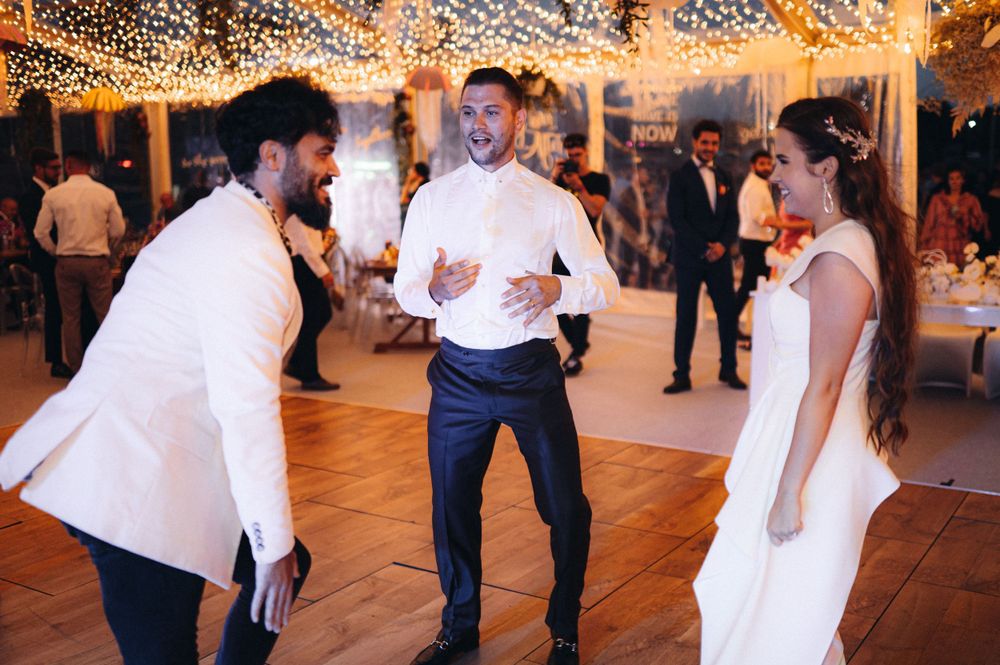 Wedding celebration with guests dancing under string lights at an outdoor reception.
