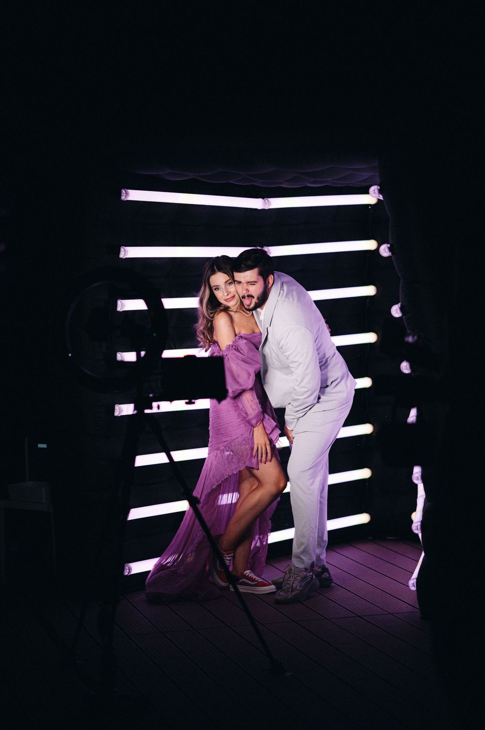 Couple poses romantically against illuminated white stripes backdrop at night event.
