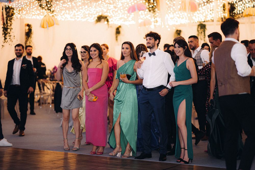 Wedding guests in colorful formal attire dancing at reception under string lights.