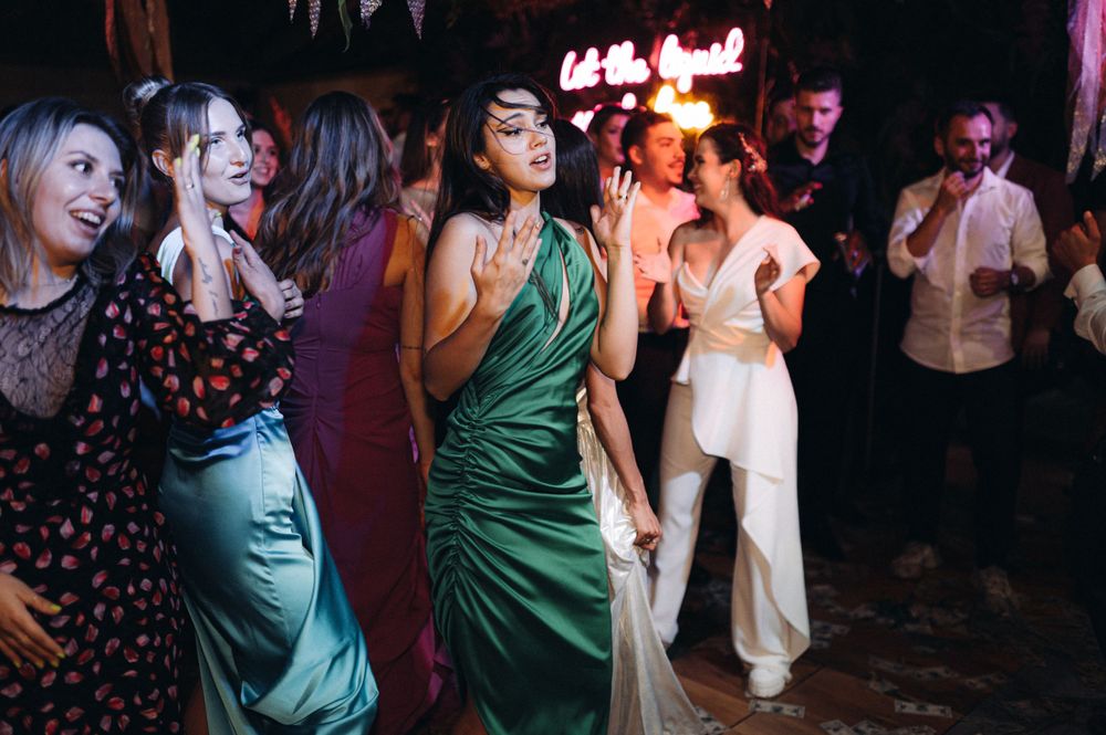 Group of party guests dancing in elegant dresses under neon lighting.