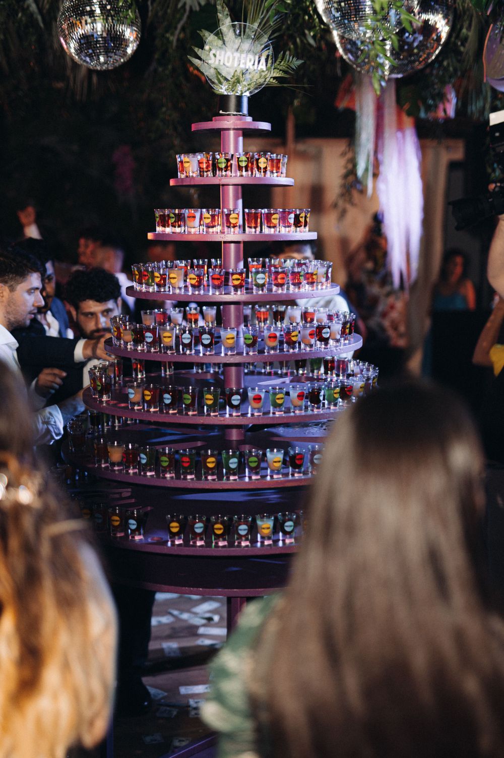 Multi-tiered display stand filled with colorful shot glasses at wedding reception.