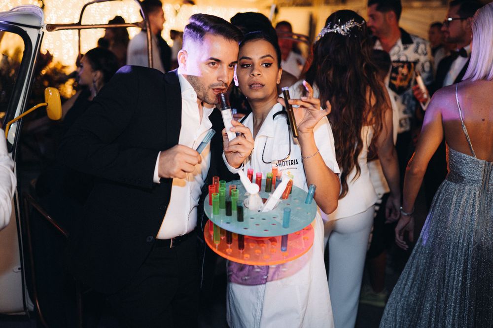 Party guests pose with colorful cake at festive indoor celebration.