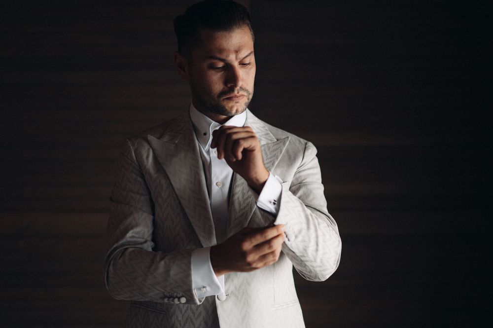 A sophisticated portrait of someone adjusting his cuffs while wearing a light colored suit.
