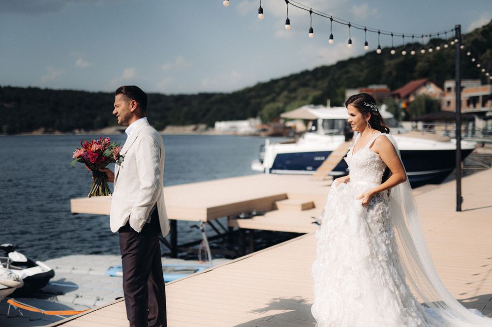 First look moment between couple at waterfront wedding venue with string lights and boats in background.