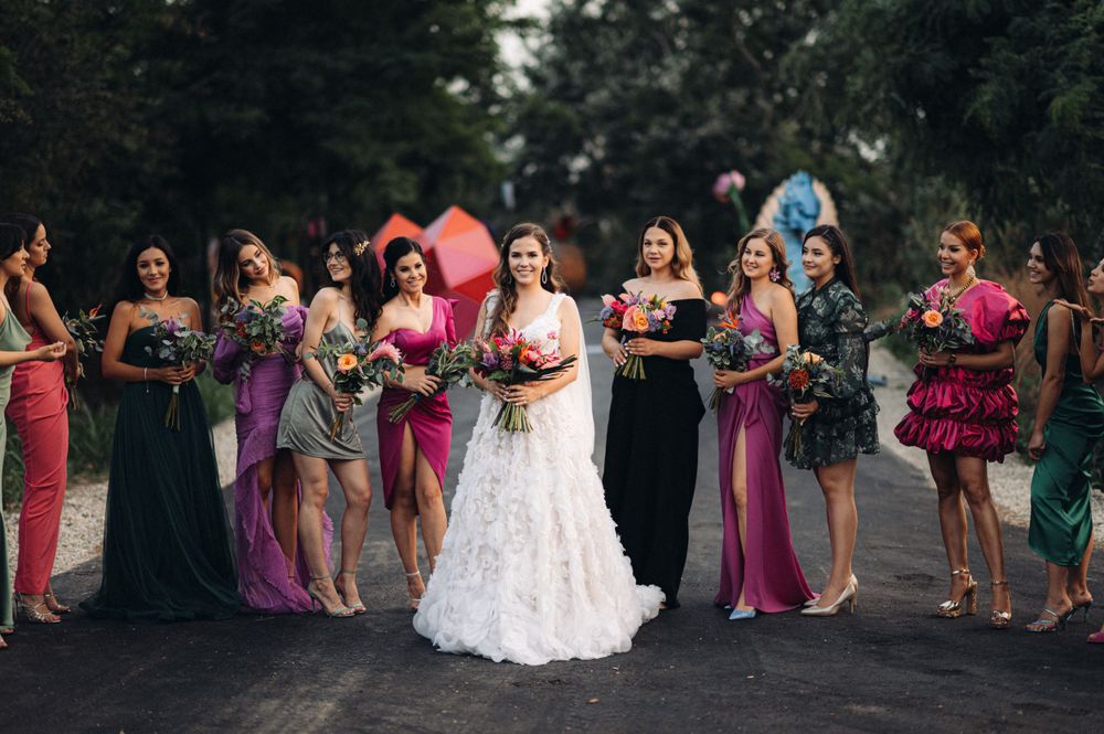 Bridal party in vibrant dresses poses for group photo outdoors.