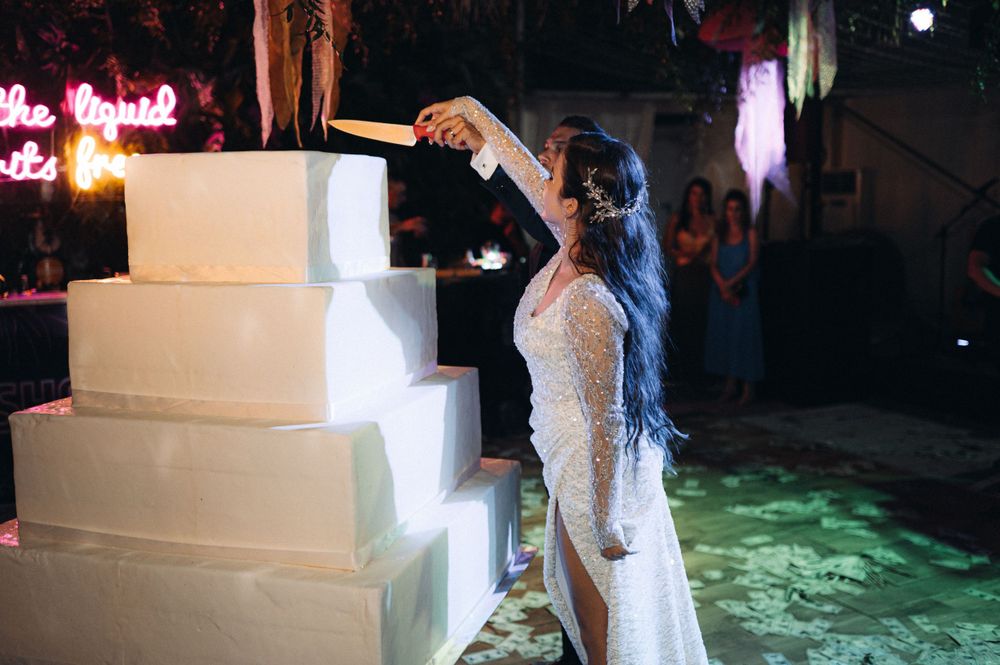 Wedding cake cutting moment with illuminated tiers in dark venue setting.