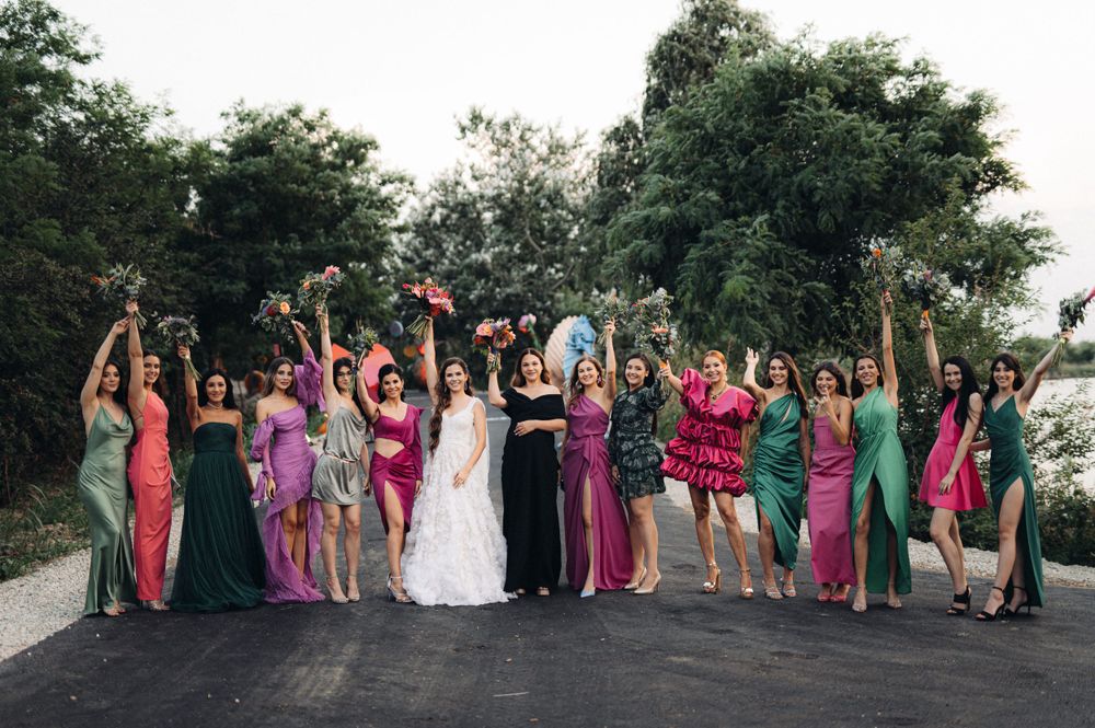 Wedding party in colorful dresses poses together on outdoor path.