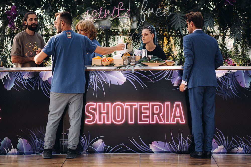 Bar setup with neon 'Shoteria' sign and purple lighting at an event venue.