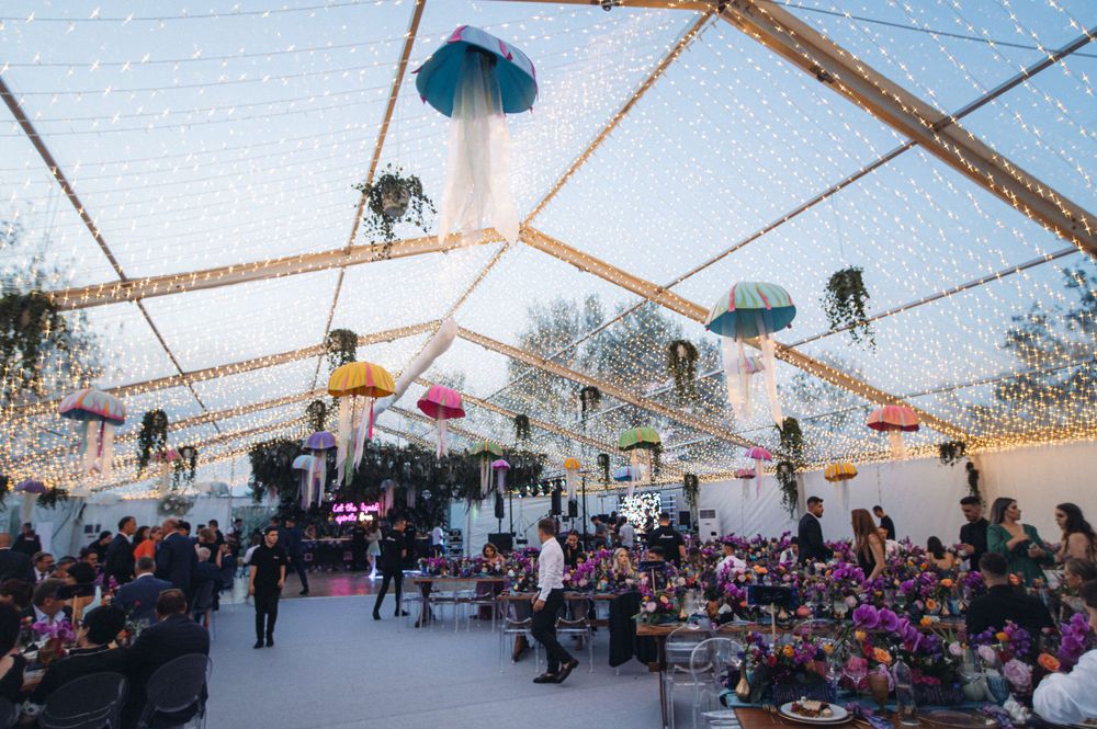 Wedding reception venue with string lights and hanging decorations under a clear tent.