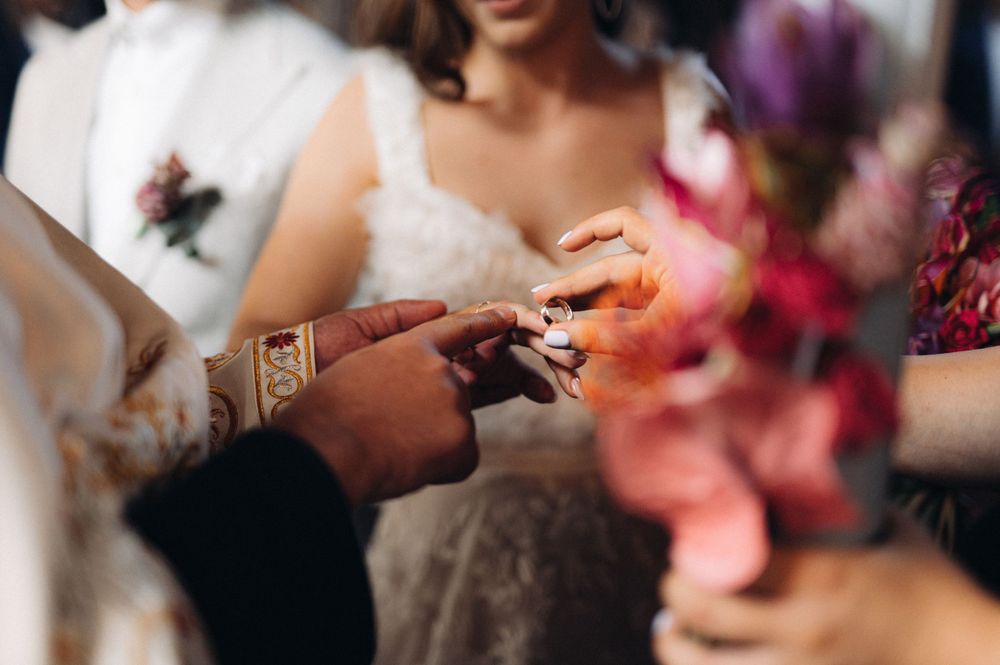 Close-up of hands exchanging rings during a wedding ceremony with pink flowers in the background.