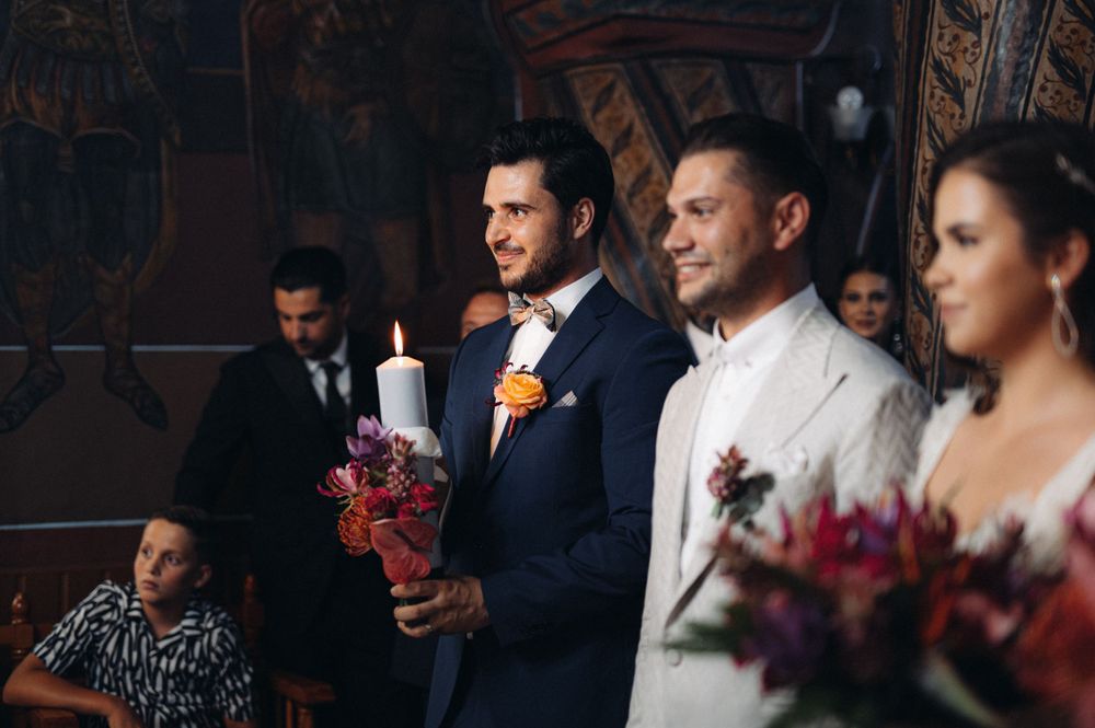 Wedding party members holding candles during a traditional ceremony with floral decorations.