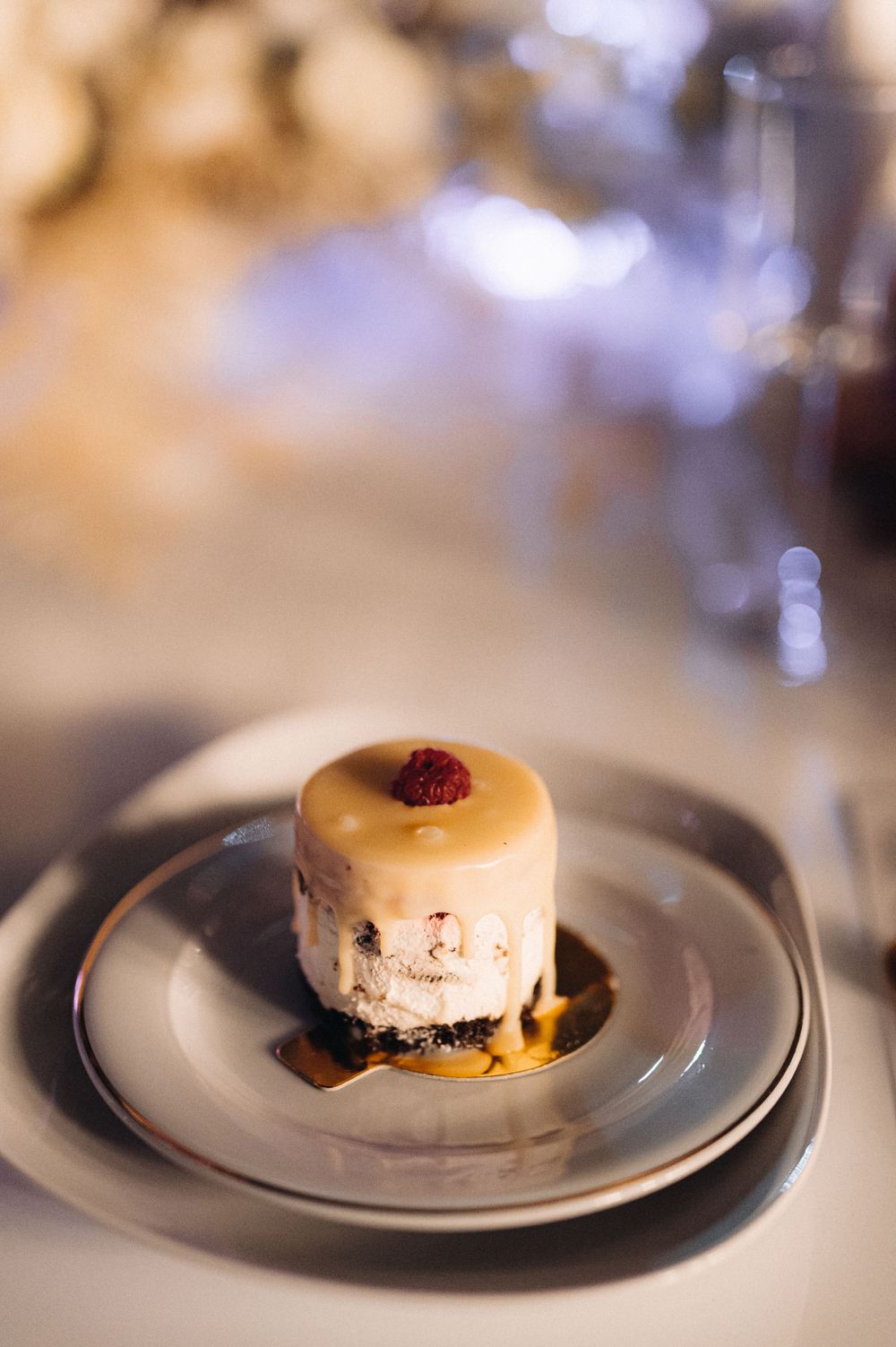 Elegant plated dessert featuring a small cake topped with raspberry on white china.