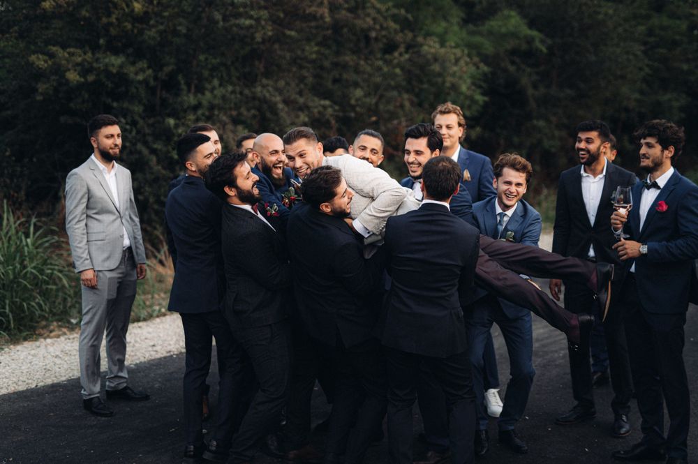 Groomsmen lift and carry someone in a playful moment during wedding photos.