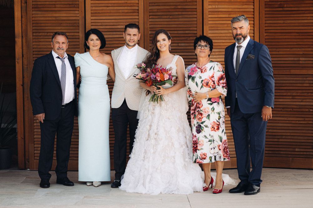 Family portrait of wedding group in formal attire against wooden panel background.
