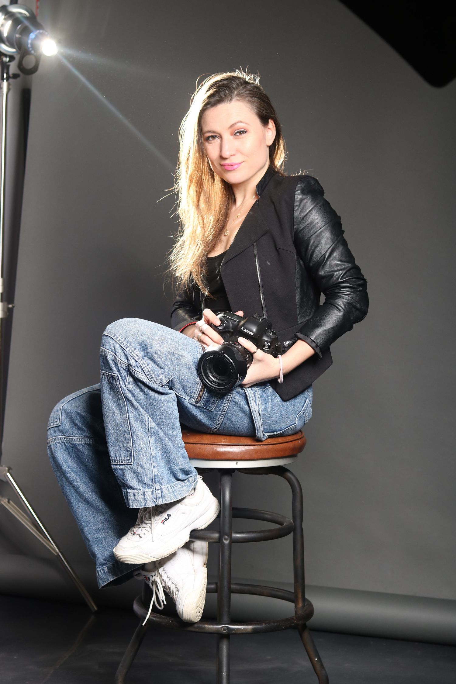Fashion portrait of someone posing on a chair against a dark background in denim and leather.