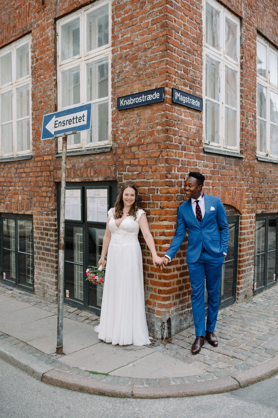 A biracial couple on their wedding day posing on Magstræde street in Copenhagen