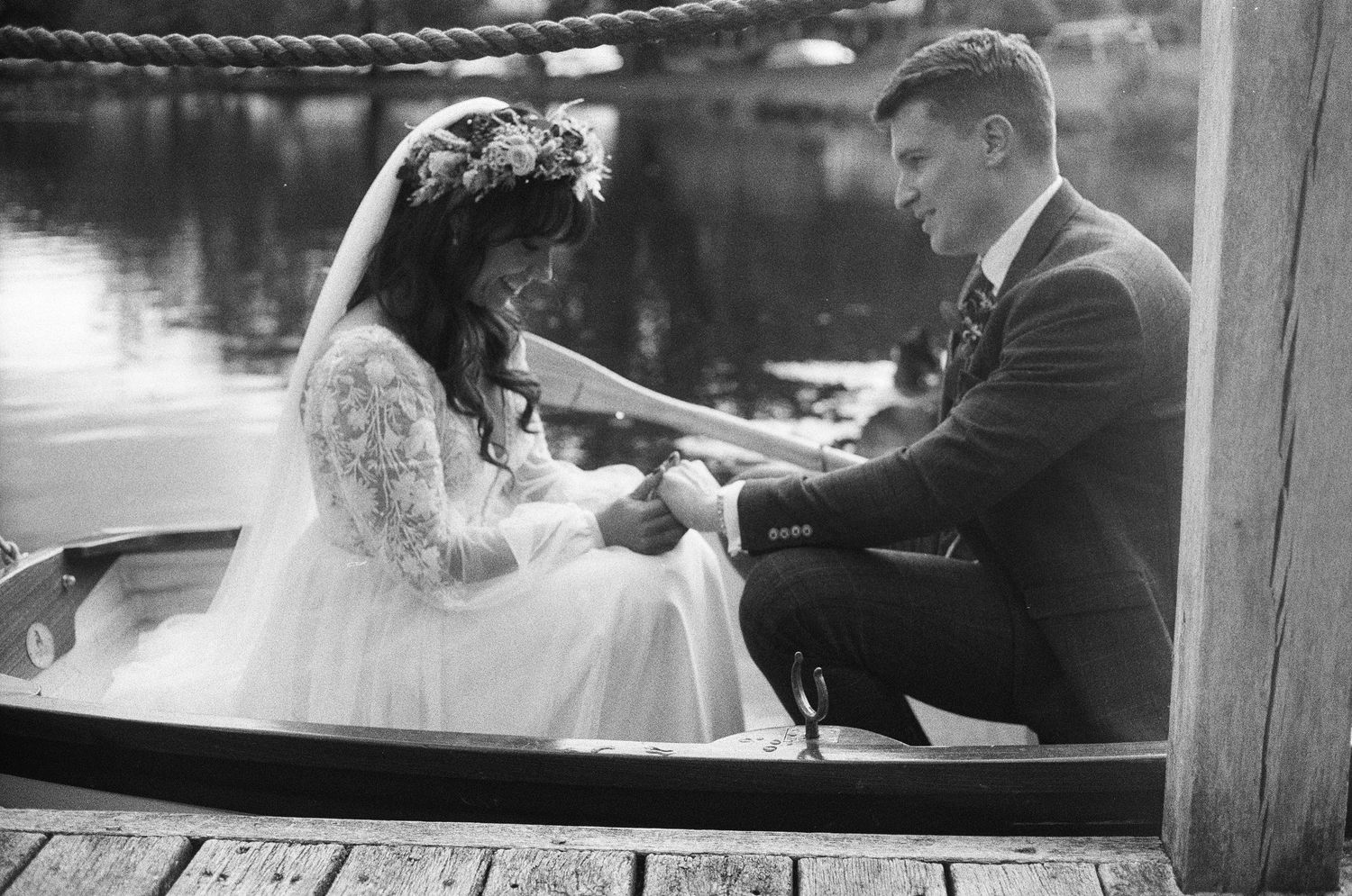 A black and white wedding photo of a couple sitting together in a rowboat on a serene lake.