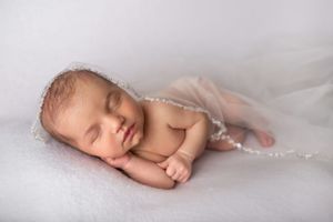 A peaceful newborn baby sleeping on soft white fabric in natural light.