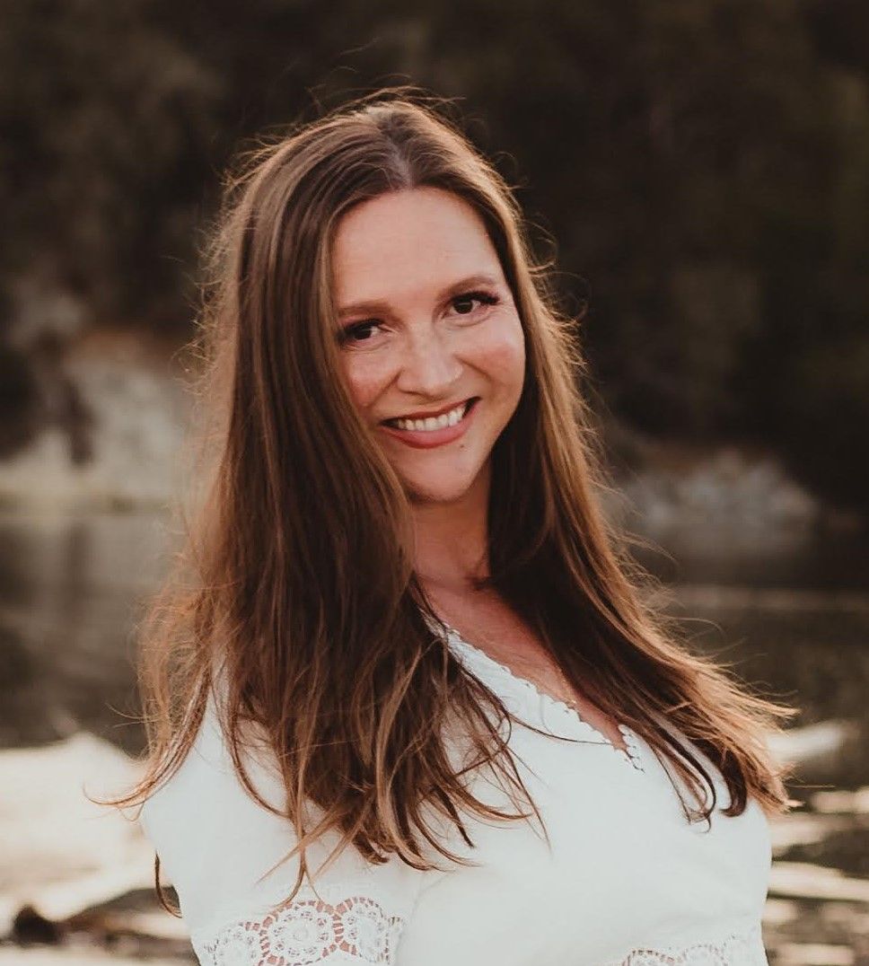 Portrait of a person with long dark hair and a radiant smile in warm sunset lighting.
