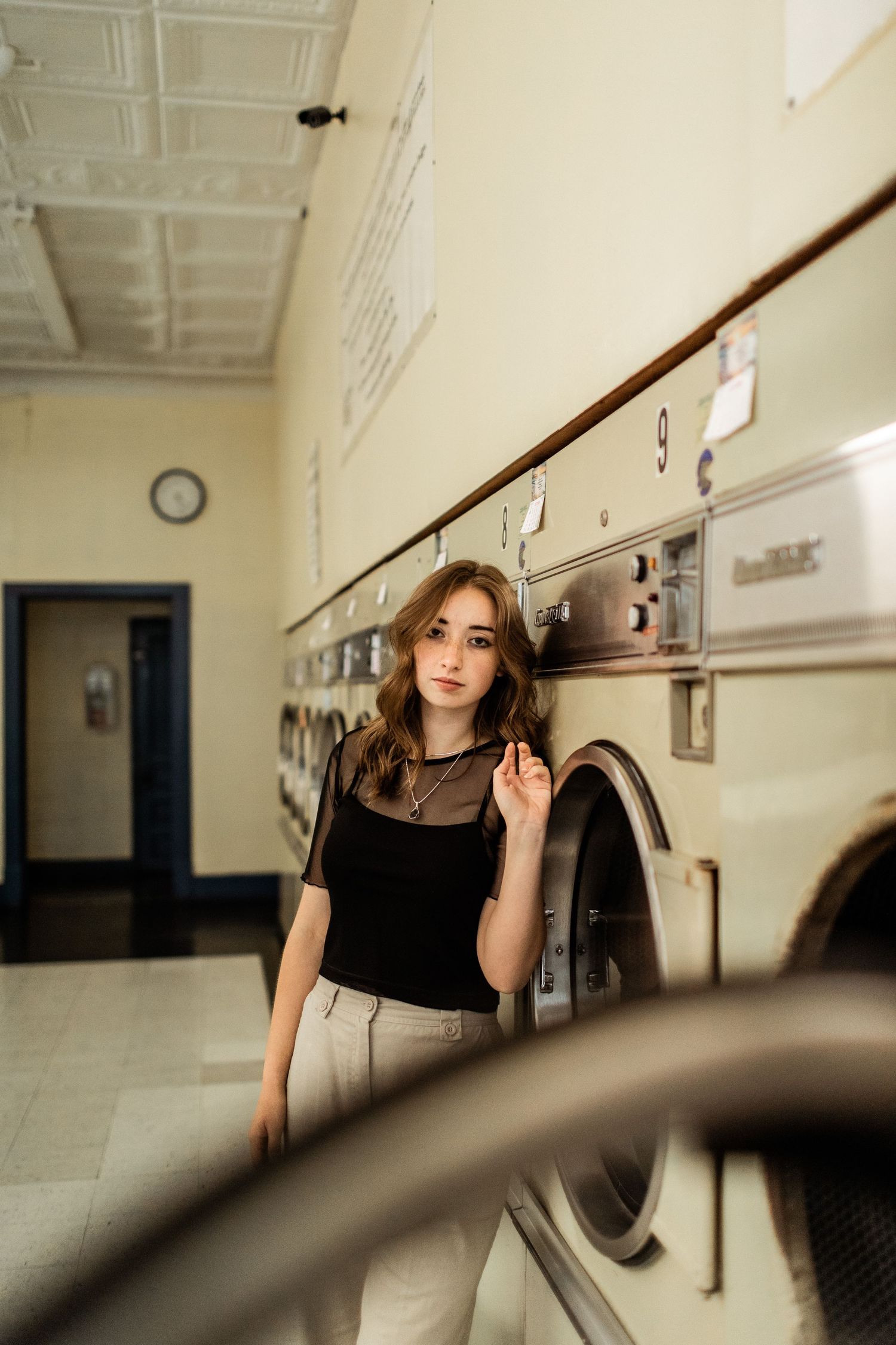 A candid portrait of a young woman posing by washing machines in a laundromat.