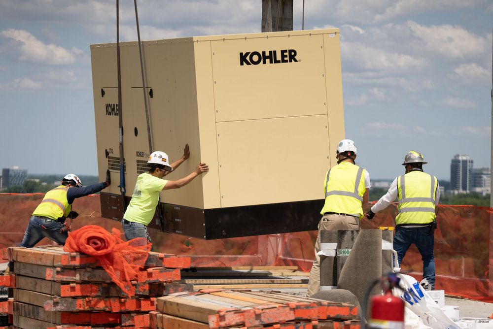 Workers in safety gear installing large Kohler equipment at construction site.