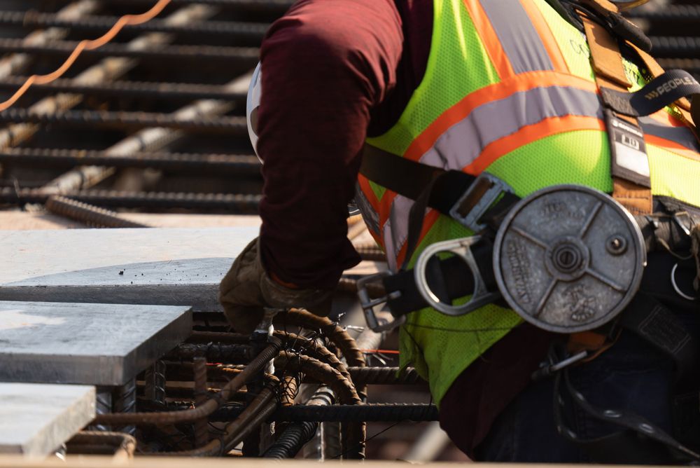 Close-up of construction work with high-visibility vest and power tool on rebar structure.