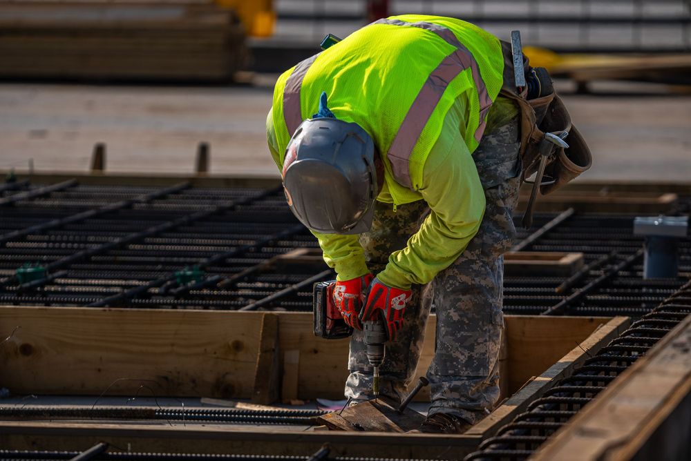 Construction worker in high-vis gear working on steel reinforcement framework.
