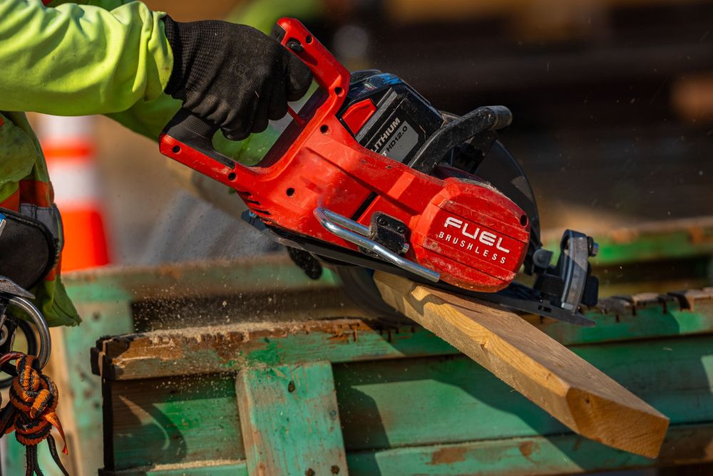 Red power tool cutting through construction materials with safety gloved hands.