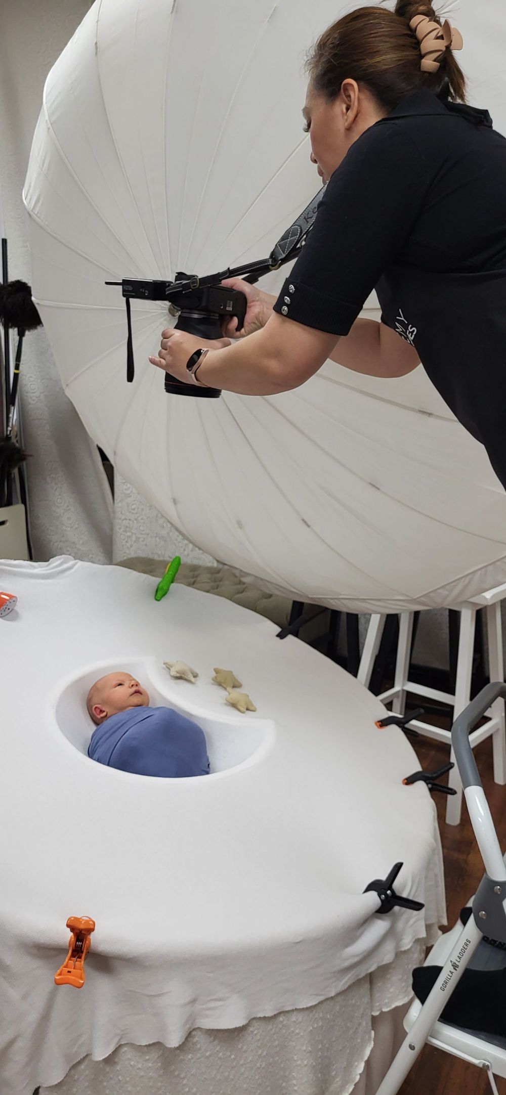 Professional photographer capturing newborn photos with large white backdrop and studio lighting.