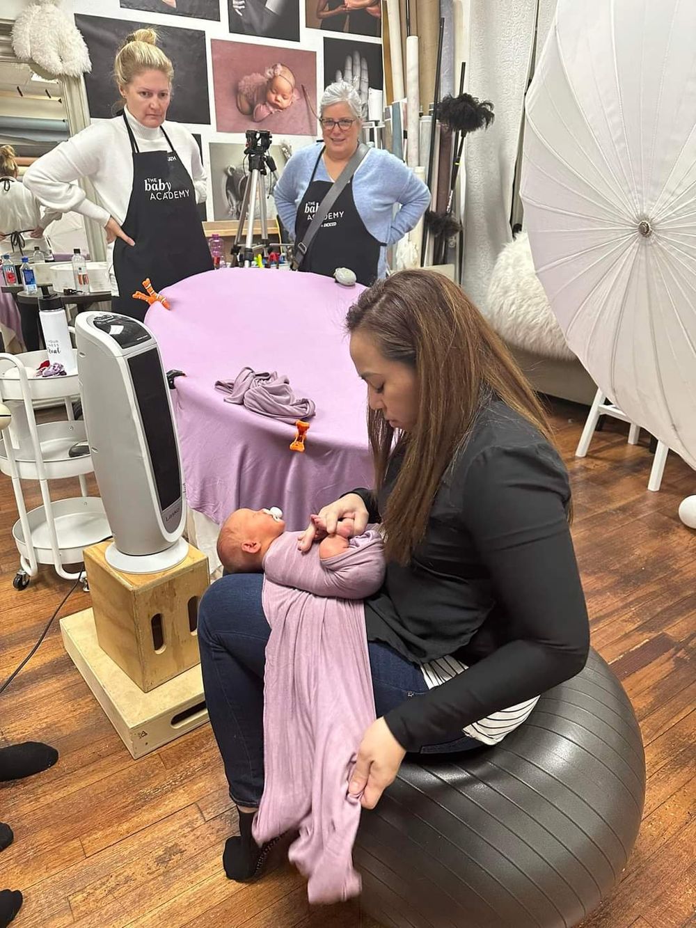 Photography studio setup with instructors and student practicing newborn photography techniques.