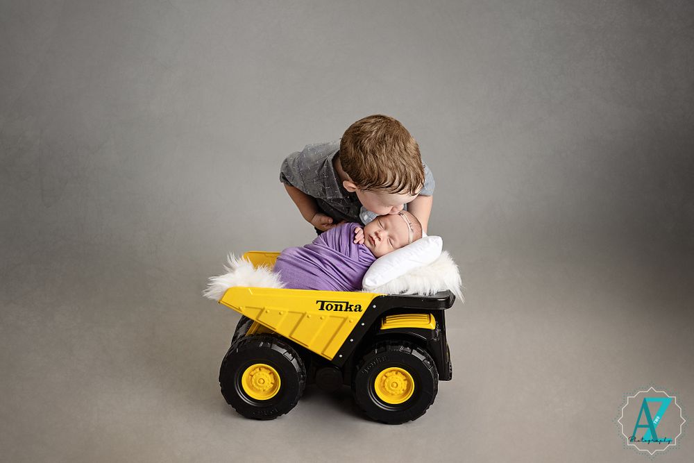 Child playing with yellow toy dump truck against grey studio background.