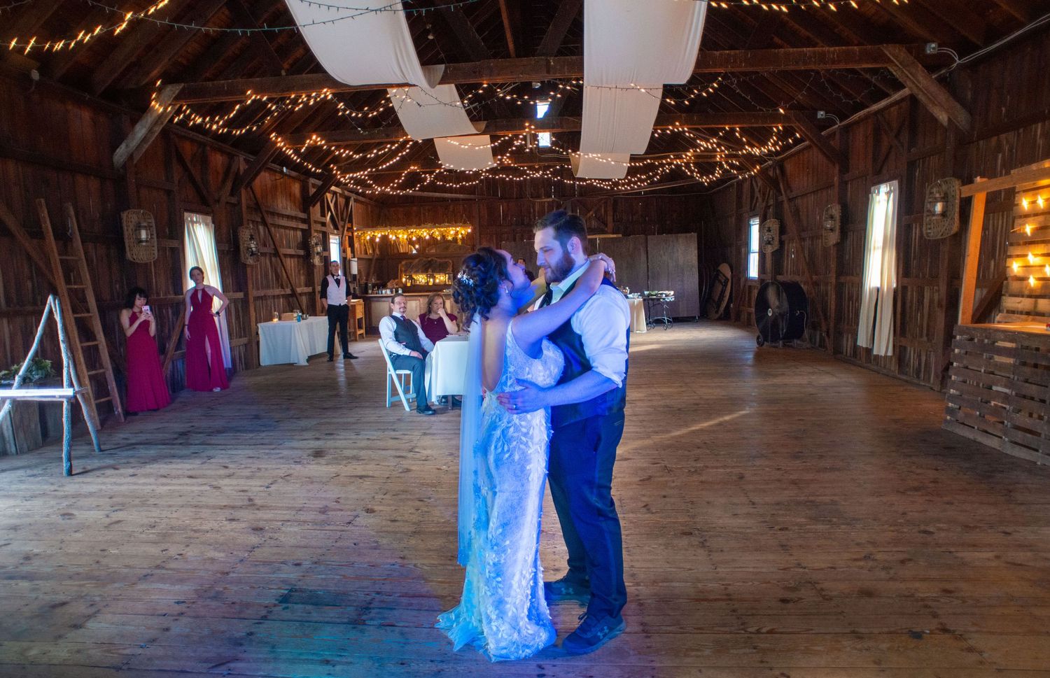 Couple shares their first dance in a rustic barn venue decorated with twinkling lights.