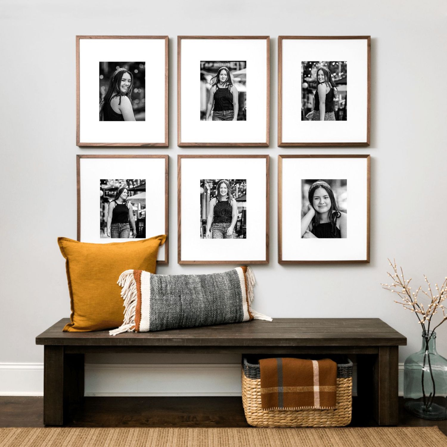 Wall arrangement of six black and white portraits above a bench with orange and gray pillows.