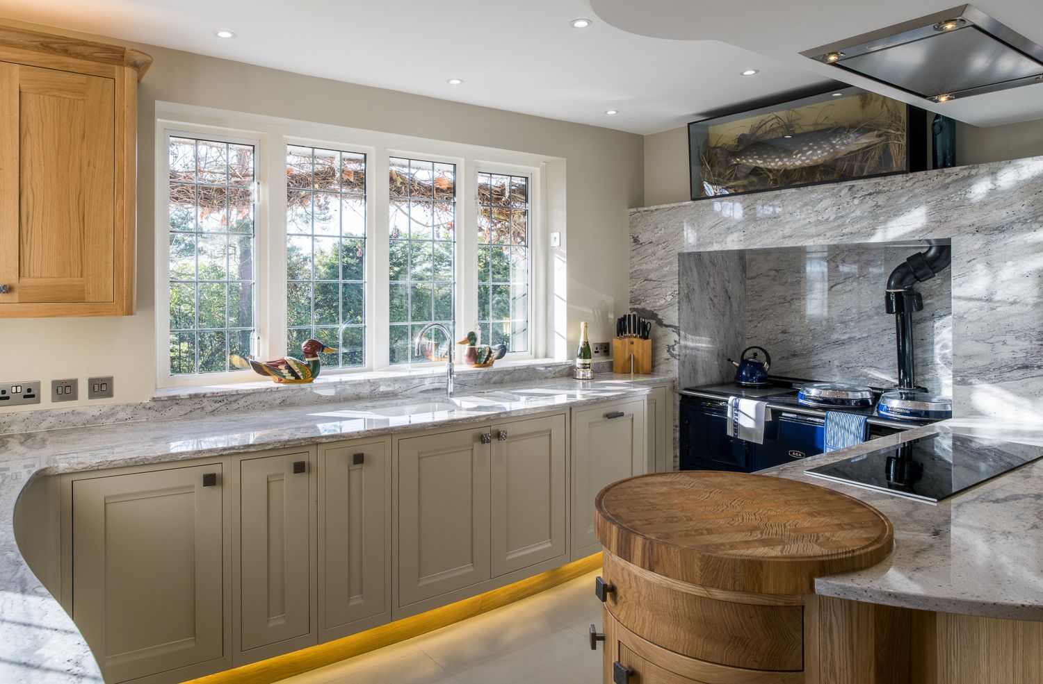 Luxurious country kitchen with beige cabinets, marble countertops, bay windows, and a black range cooker with dramatic backsplash.
