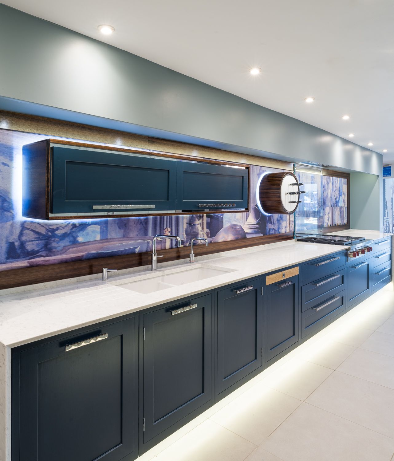 Modern navy blue kitchen cabinets with white countertops, LED lighting, and a reflective blue backsplash.