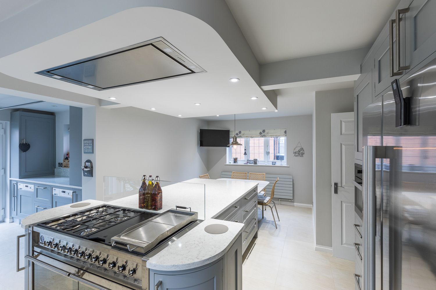 Modern white kitchen interior with stainless steel appliances, curved countertop, and ceiling-mounted range hood.