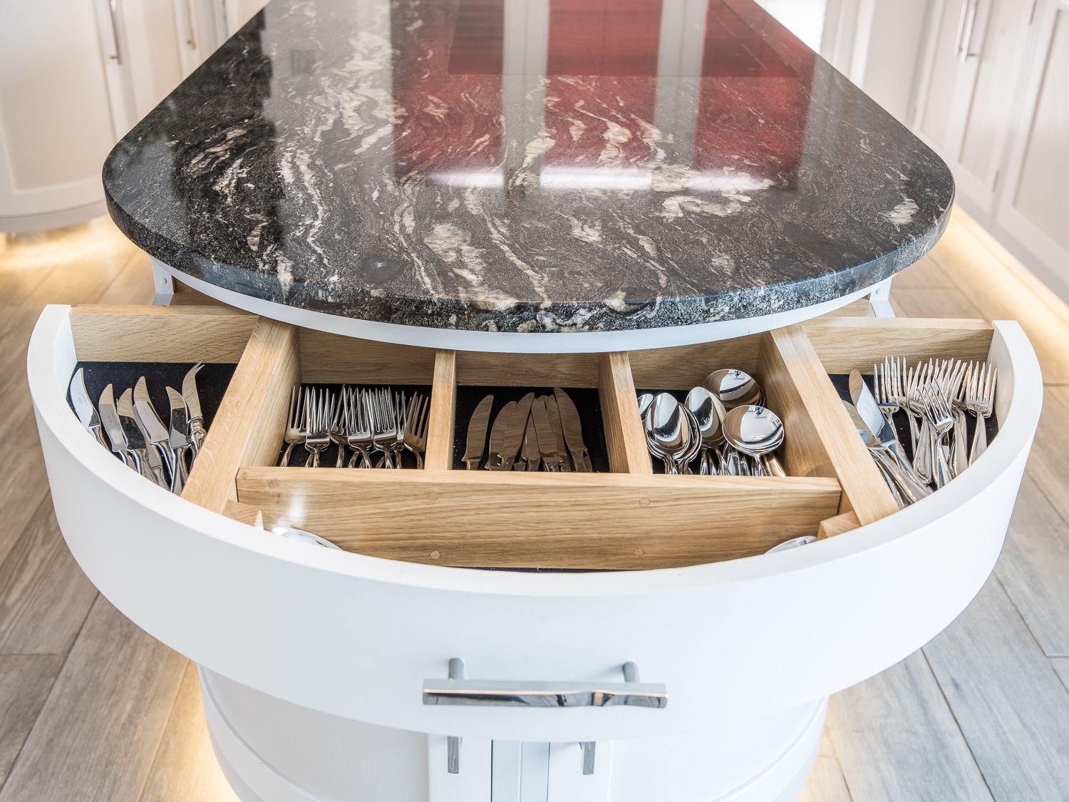 Modern round table with built-in circular drawer compartment holding organised silverware and utensils.