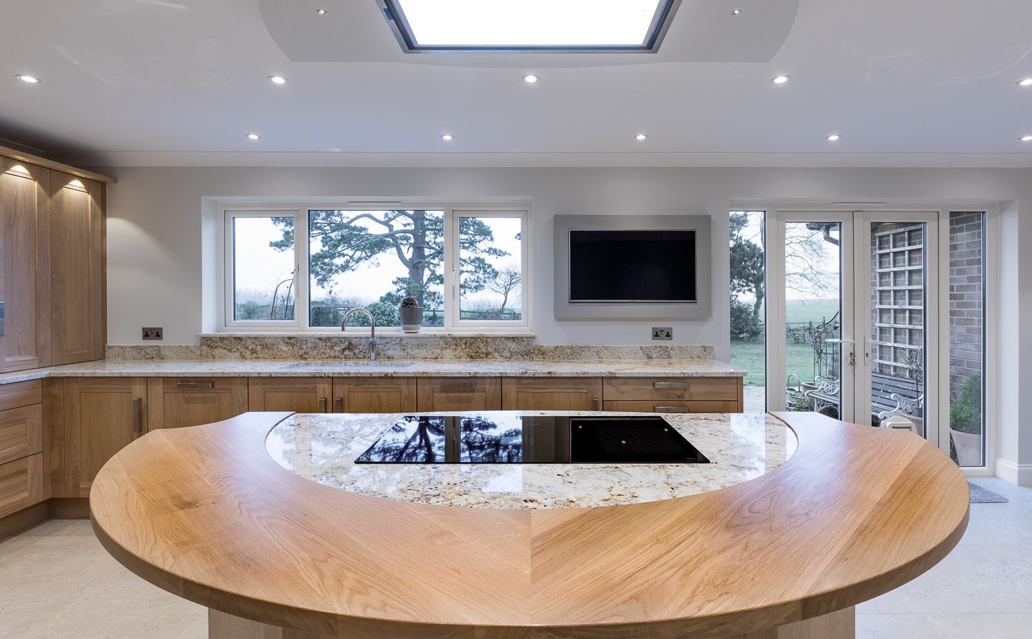 Modern curved wooden kitchen counter with built-in lighting and white cabinetry in a luxury home interior.