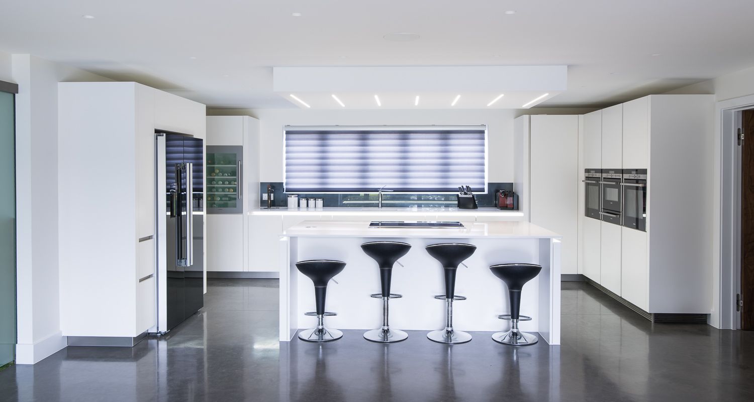 Modern white kitchen with minimalist design featuring a sleek island bar and four black bar stools against polished floors.