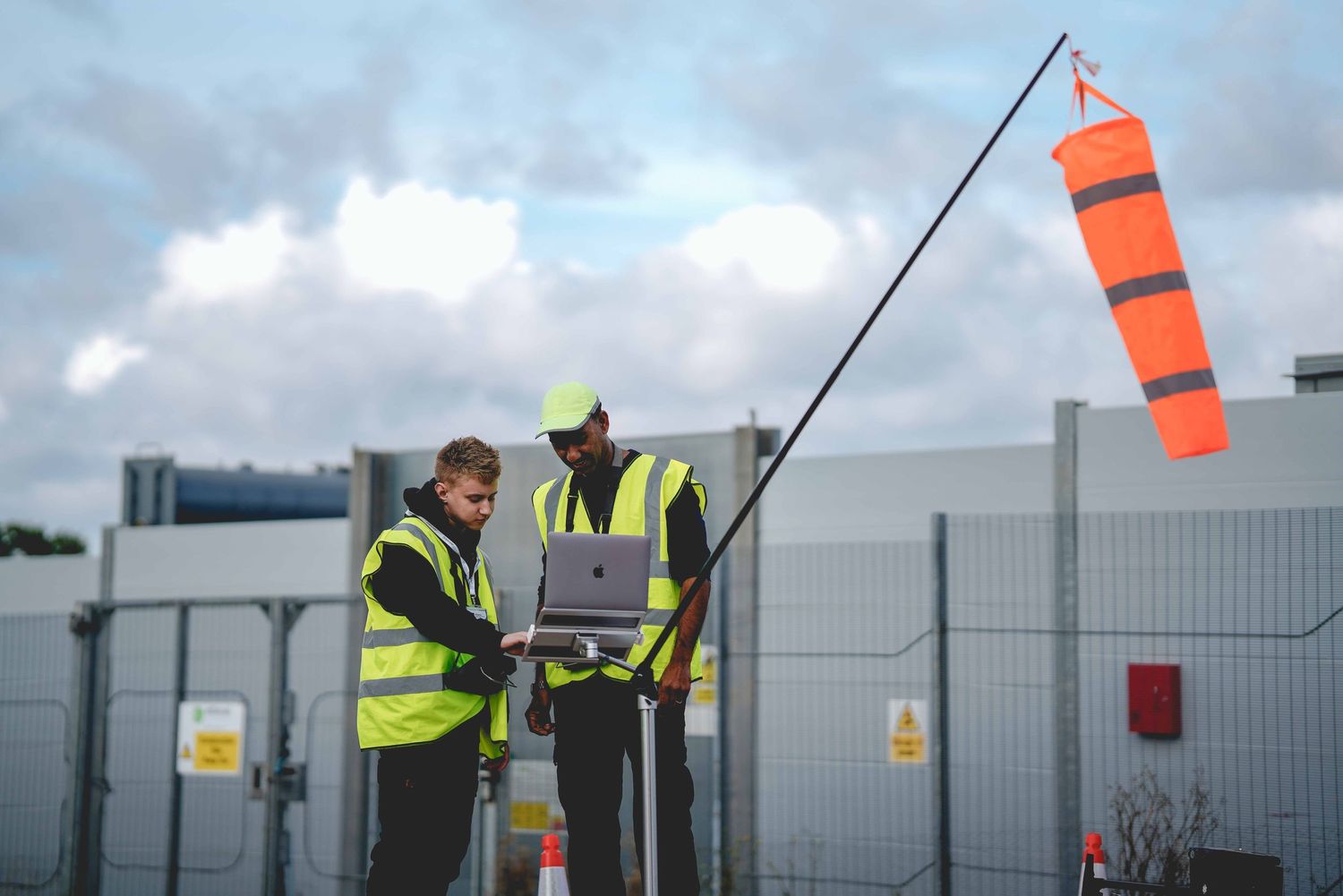 Workers in high-visibility vests checking wind conditions with an orange windsock.