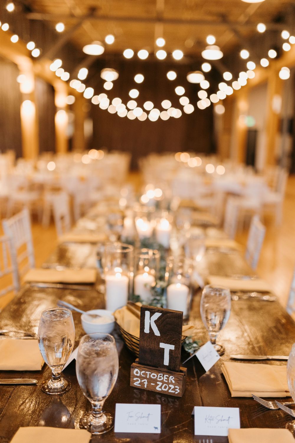 Wedding sweetheart table with KT monogram sign, candles, string lights, and gold place settings.
