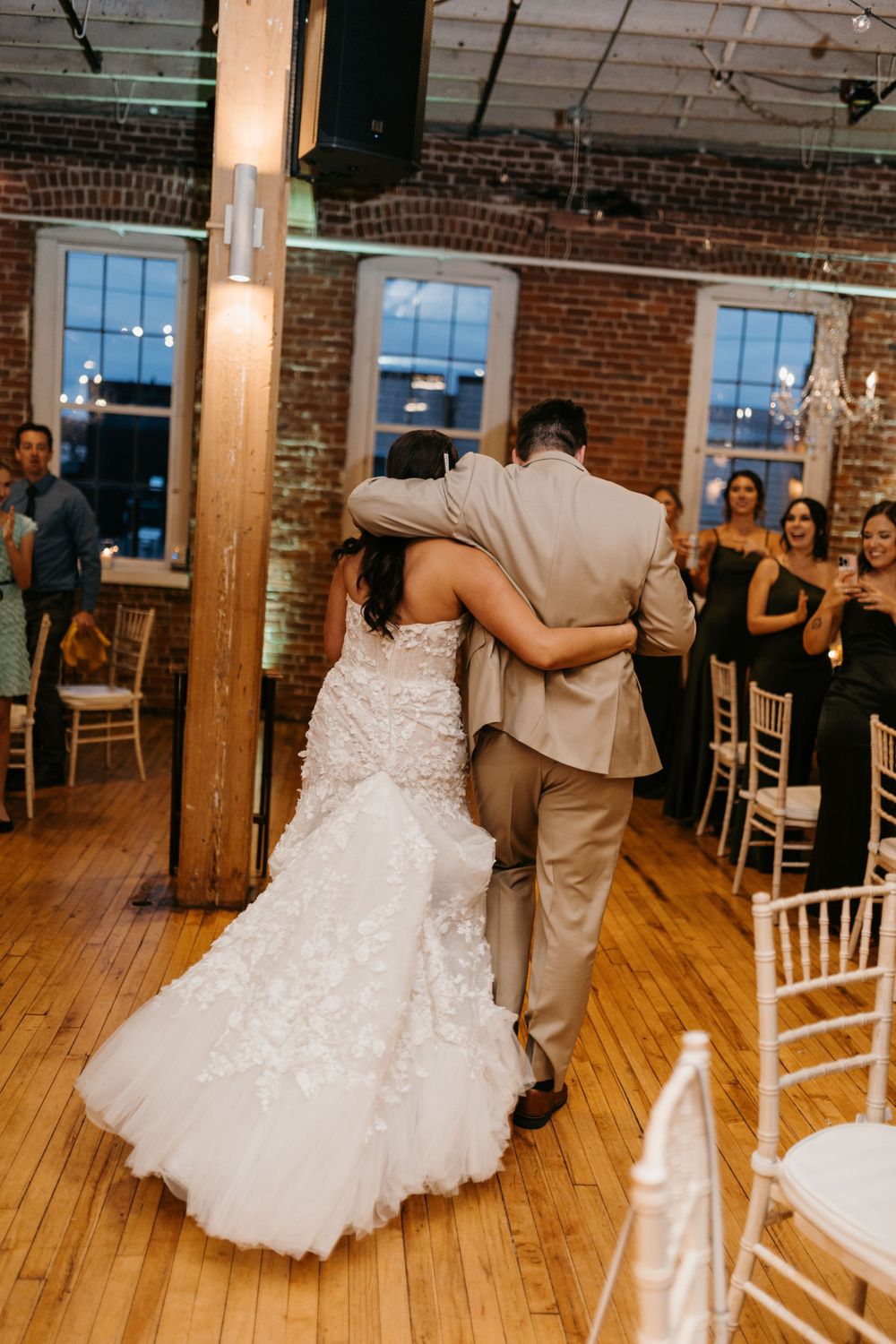 Bride and groom share intimate first dance in elegant rustic wedding venue with brick walls.