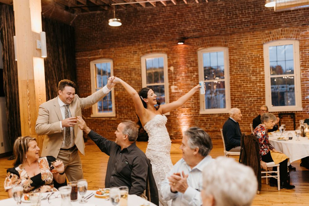 Joyful bride and groom celebrate grand entrance at rustic brick-walled wedding reception.
