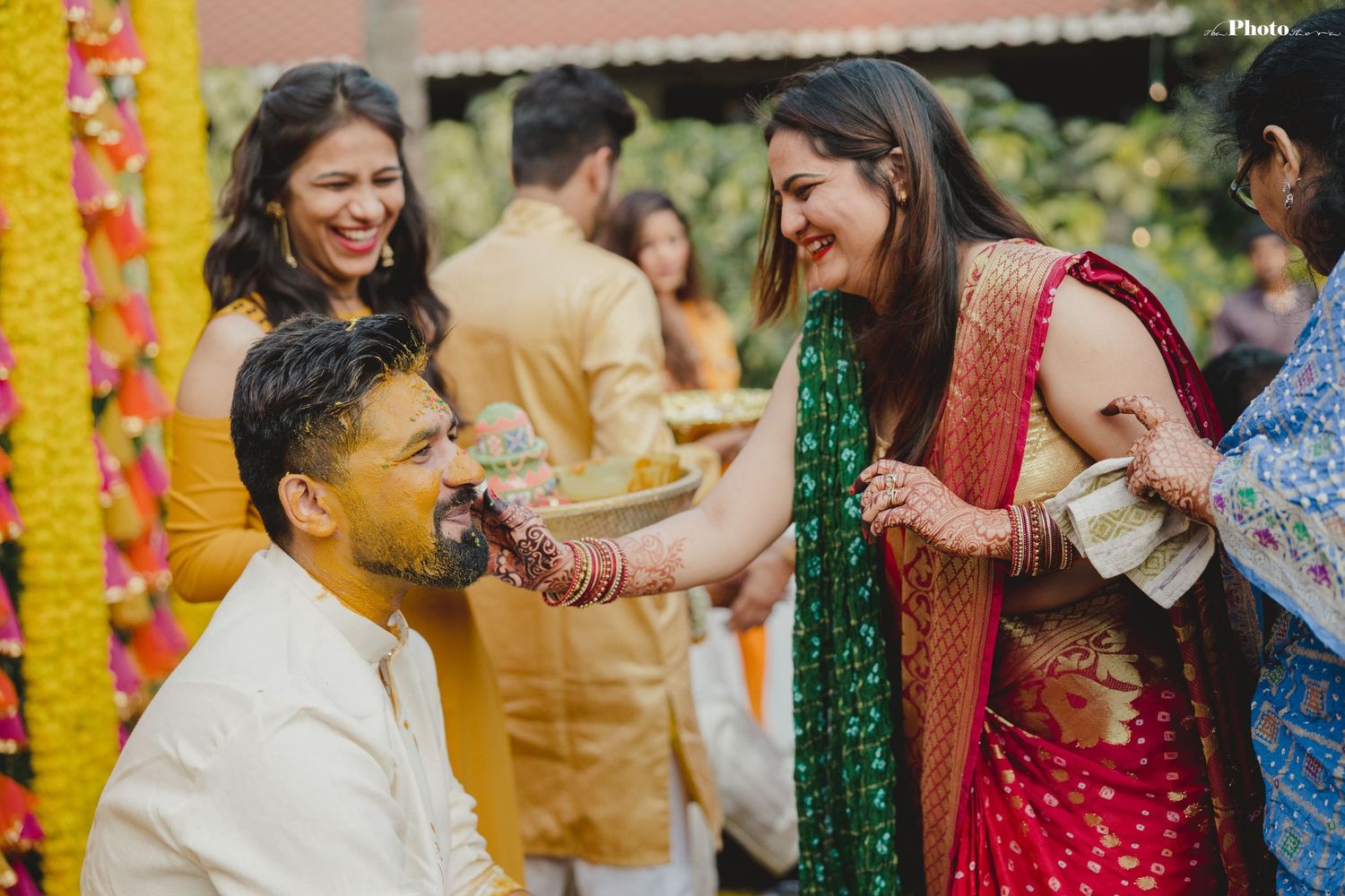 Guests participate in traditional pre-wedding rituals with yellow marigold decorations in background.