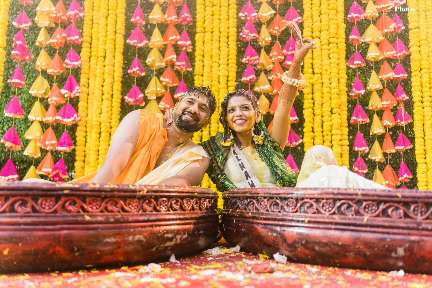 Ornate wedding stage decorated with yellow marigold garlands and pink floral elements against a decorated backdrop.